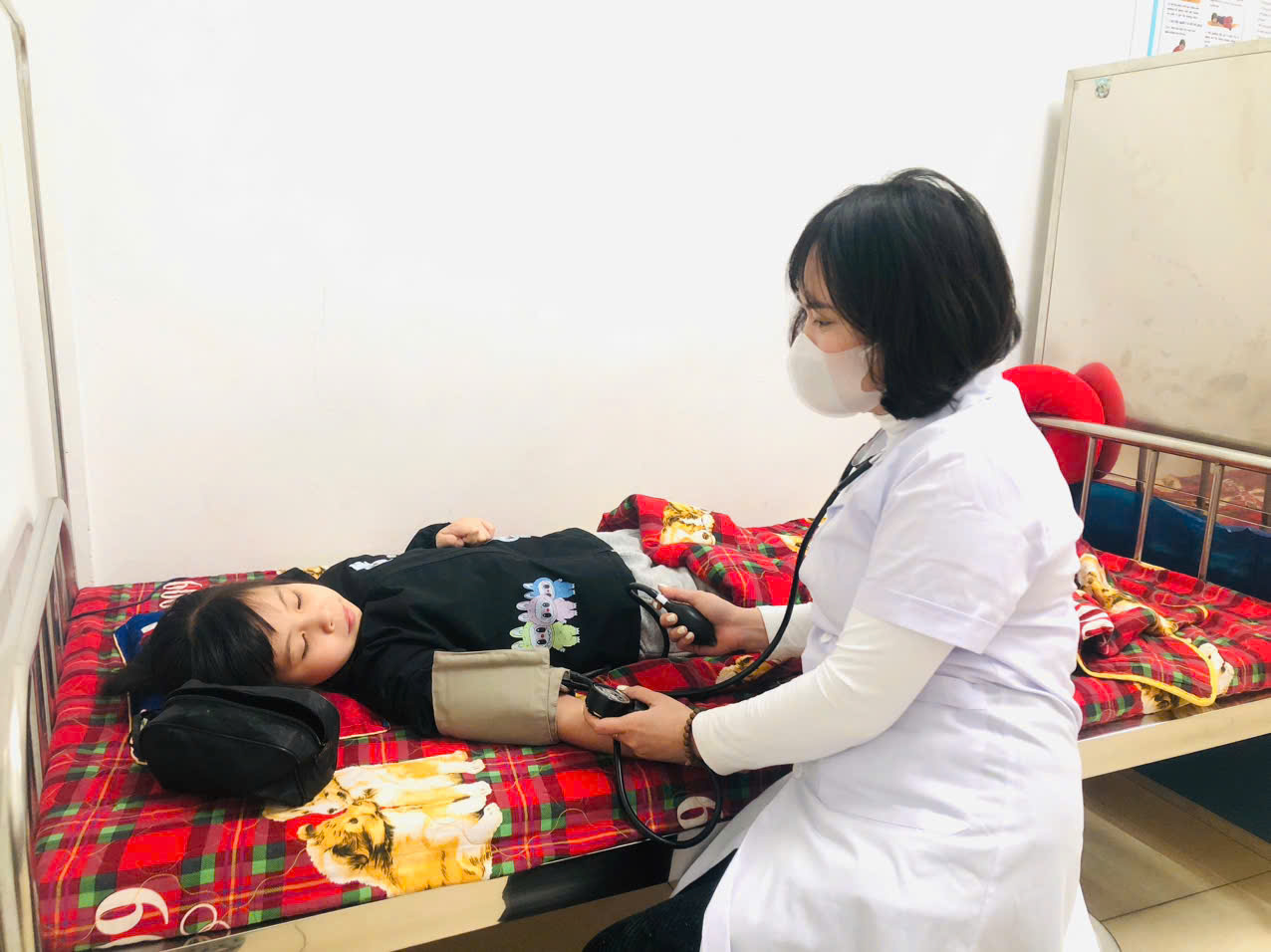 A person wearing a white coat and a mask examining a child's blood pressure

AI-generated content may be incorrect.