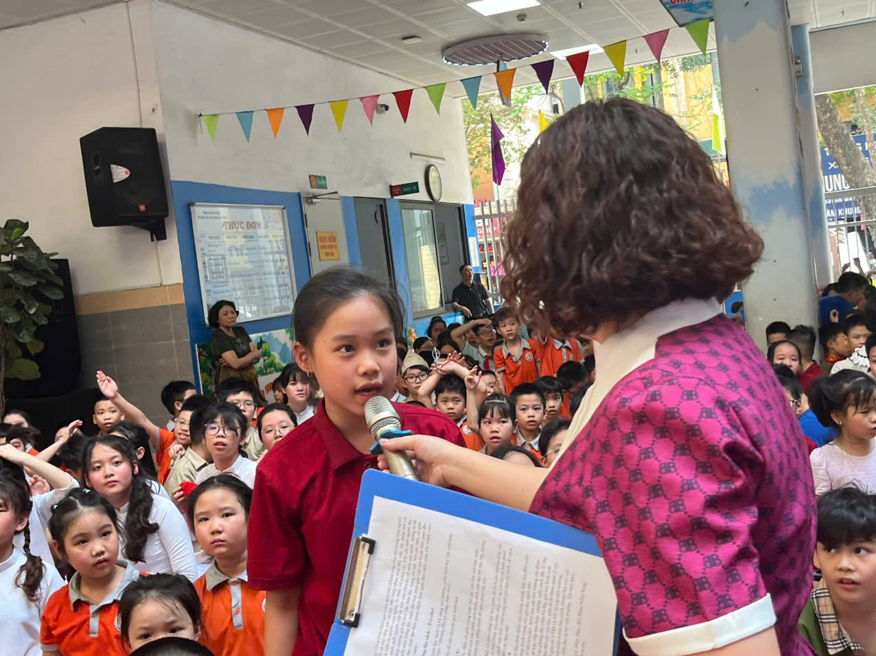 A person holding a microphone and speaking to a child in a classroom

AI-generated content may be incorrect.